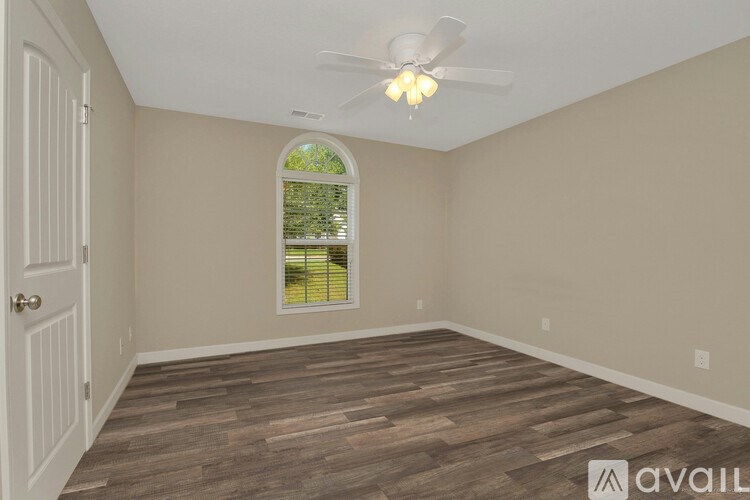 A room with a ceiling fan and a window with a view of greenery outside.