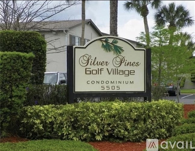 A sign for Silver Pines Golf Village Condominium 5505 surrounded by green bushes.