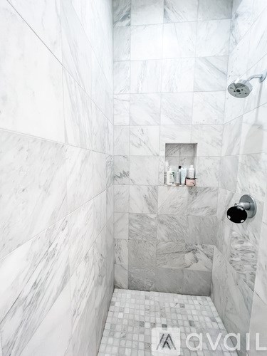 A white marble bathroom with a shower and a small shelf.