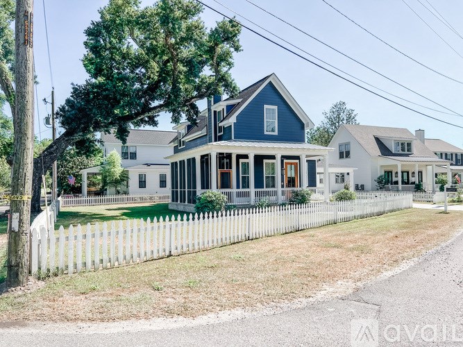 A white picket fence surrounds a two-story house with a blue roof.