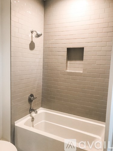 A white bathtub with a shower head and a square drain in a tiled bathroom.