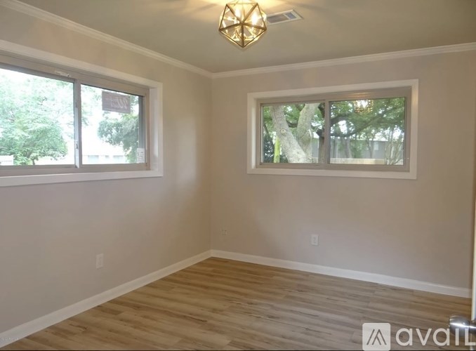 A room with wooden flooring and two windows.