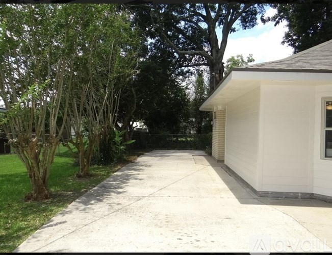 A white house with a driveway and trees in the background.