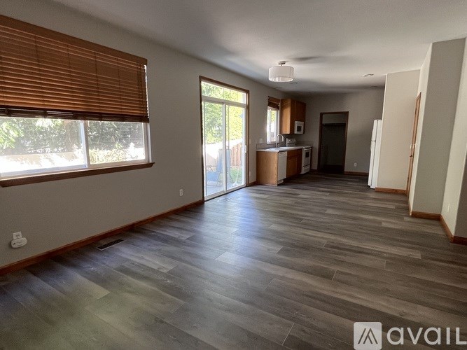 A spacious room with wooden flooring and a large window with blinds.