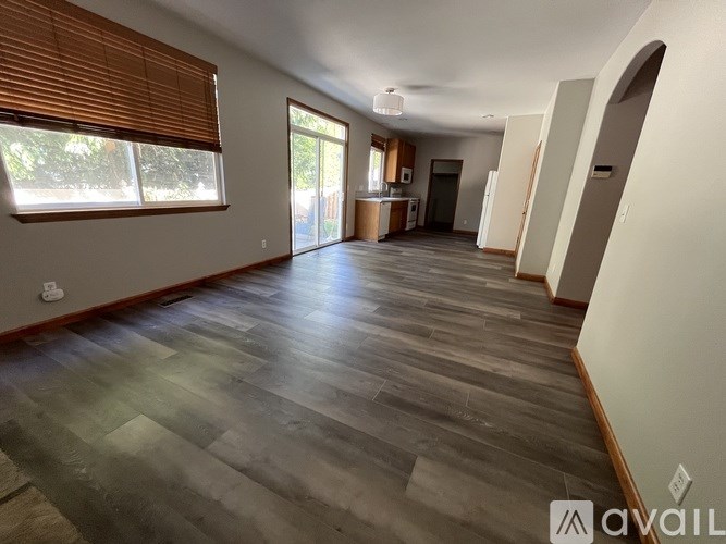 A spacious room with wooden flooring and a large window with blinds.