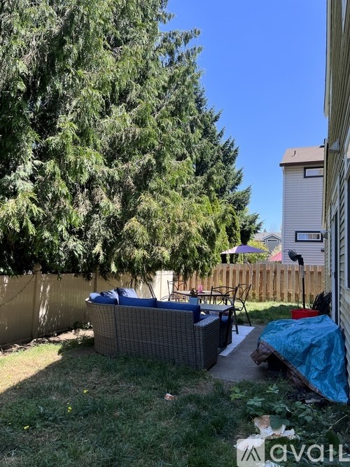 A backyard with a fence, a tree, and a patio set.