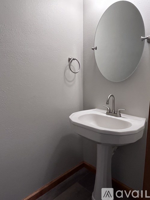 A white pedestal sink with a round mirror above it.