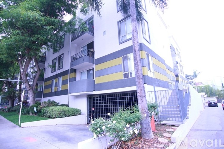 A modern building with a white and yellow facade is surrounded by greenery.
