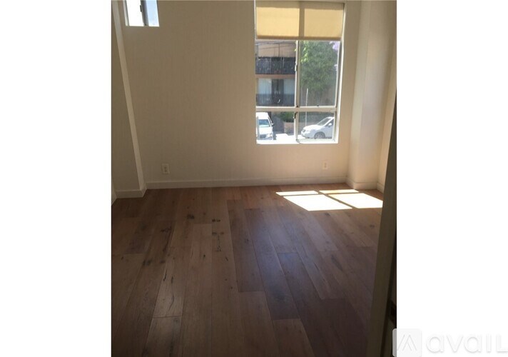 A room with wooden flooring and a window showing a parking lot outside.