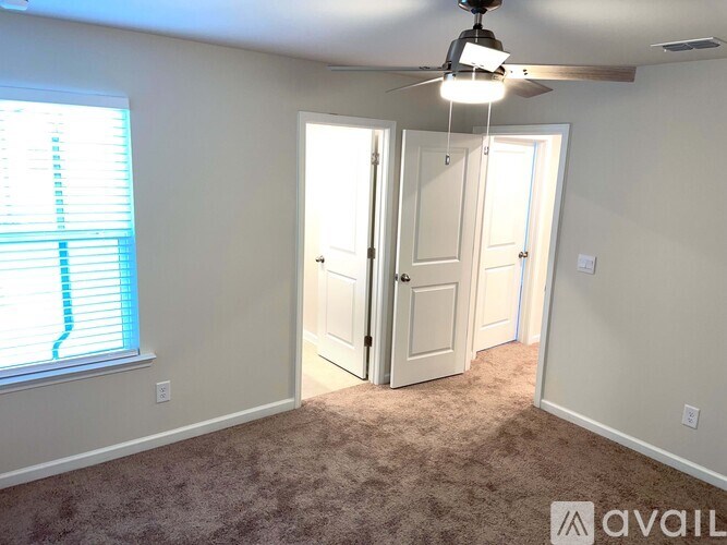 A room with a carpeted floor, a ceiling fan, and a window with blinds.