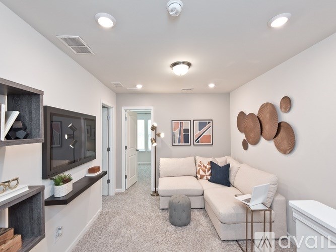 A modern living room with a white couch, a grey ottoman, a white chair, a TV on the wall, and a painting.