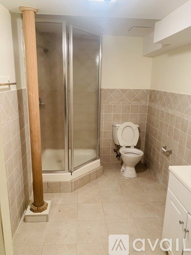A bathroom with a toilet, a wooden column, and a glass shower door.