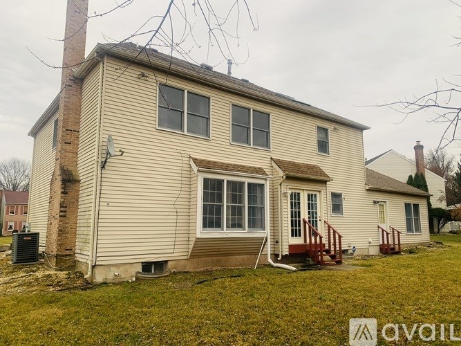 A house with a beige siding and a red door is surrounded by a grassy area.