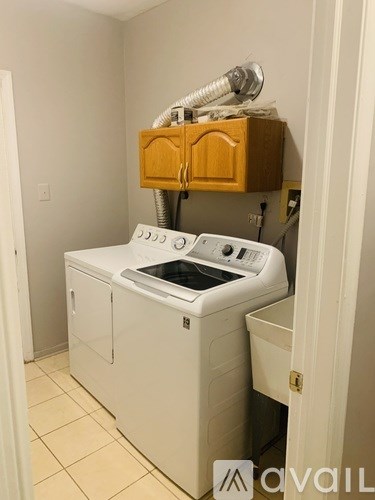 A washing machine is in a small room with a ventilation pipe above it.
