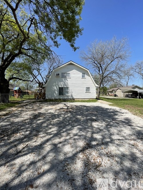 A white barn sits in the middle of a driveway with trees on either side.
