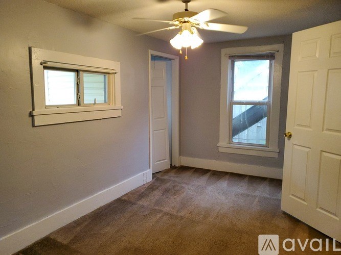 A room with a ceiling fan and two windows.