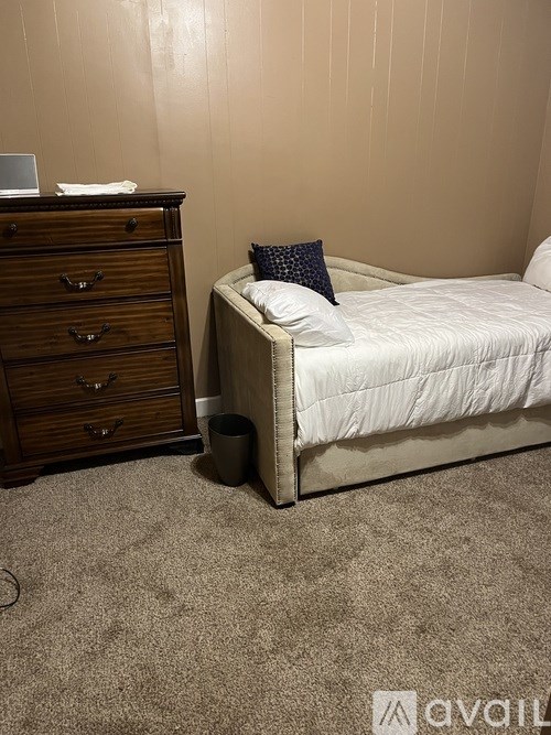 A bedroom with a bed, dresser, and trash can.