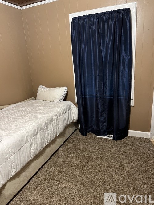 A bedroom with a bed, pillow, and a curtain.