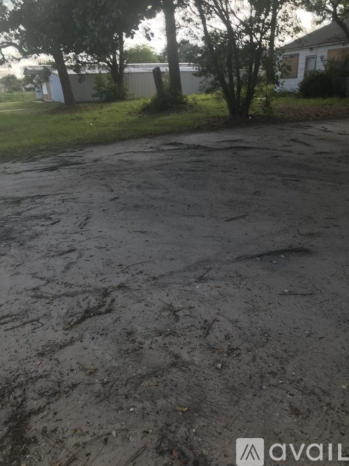 A muddy parking lot with a house and trees in the background.
