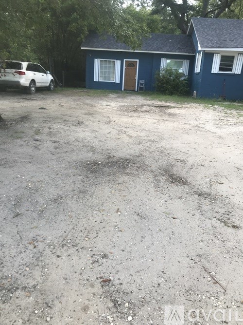 A white car is parked in front of a blue house.