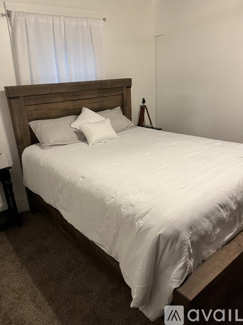 A bed with a white comforter and two pillows sits in a room with a carpeted floor.