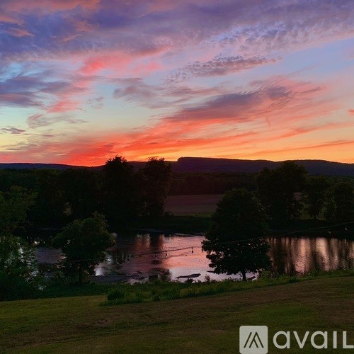 A beautiful landscape with a lake, trees and hills under a colorful sky.