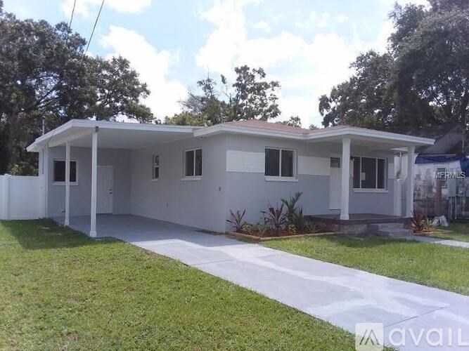 A white house with a red roof is surrounded by greenery.