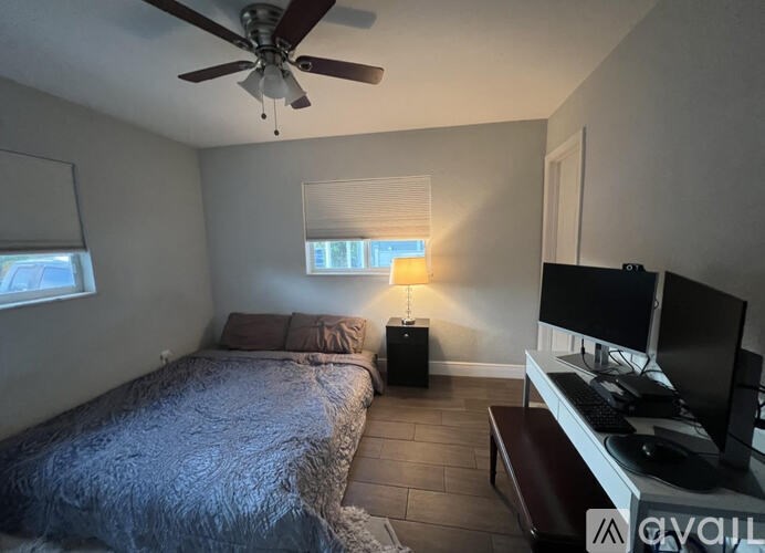 A bedroom with a bed, a desk with a computer, and a ceiling fan.