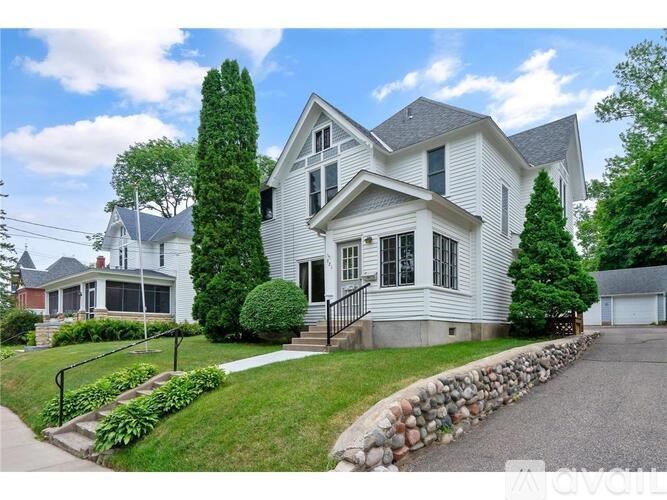 A large white house with a grey roof and a stone wall in front.
