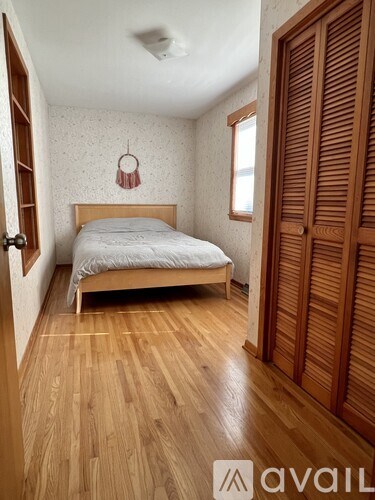 A bedroom with a bed, wooden floor, and a wall with a patterned wallpaper.