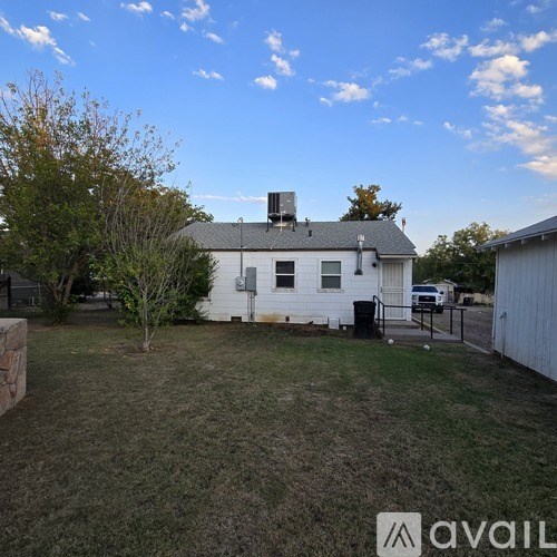 A white house with a grey roof and a chimney is surrounded by a grassy yard.