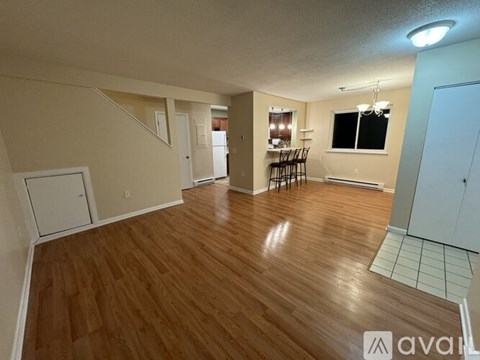 A room with wooden flooring and a kitchen area in the background.