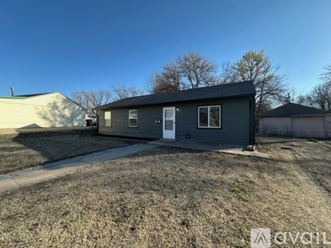 A grey house with a white door and windows is surrounded by a grassy area.