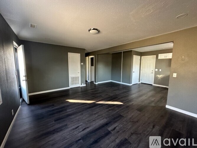A spacious room with wooden flooring and multiple doors.