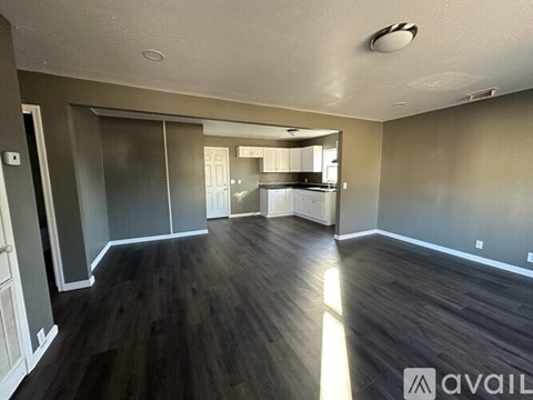 A spacious room with wood flooring and a kitchen in the background.