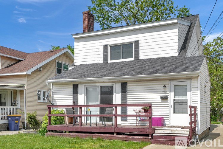 A white house with a red deck and a blue trash can.