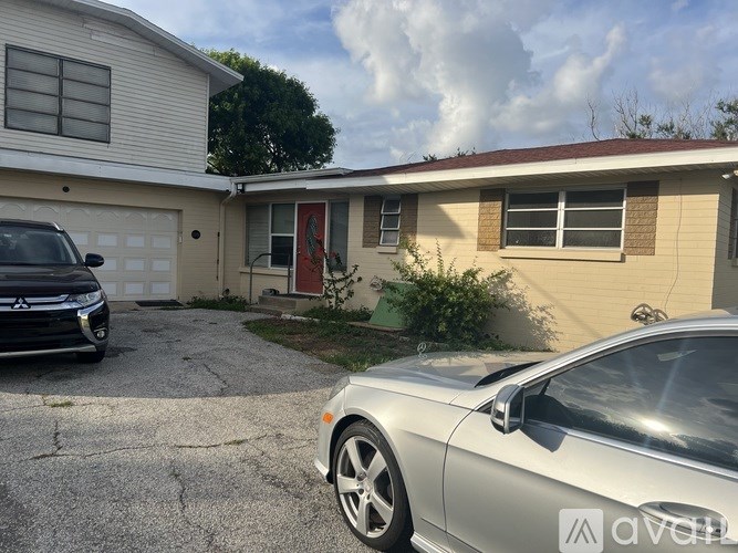 A silver car is parked in front of a house with a red door.
