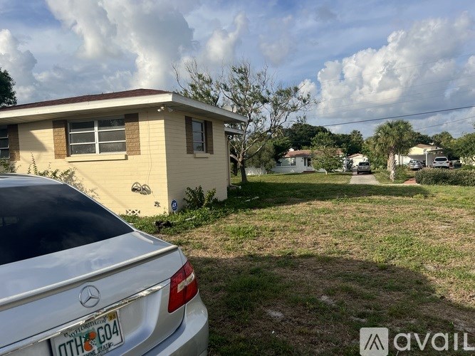 A white Mercedes car is parked in front of a yellow house.