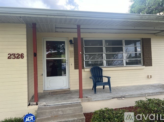 A blue chair is on the porch of a house with the number 2326 on it.