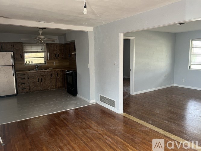 A room with wooden floors and a kitchen area in the background.
