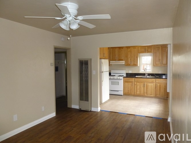 A room with a ceiling fan and a kitchen area in the background.