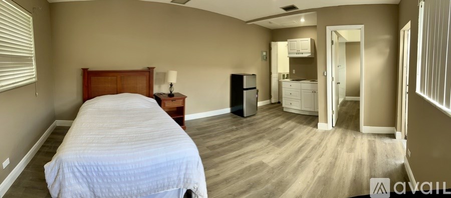 A bedroom with a bed, dresser, and a refrigerator.