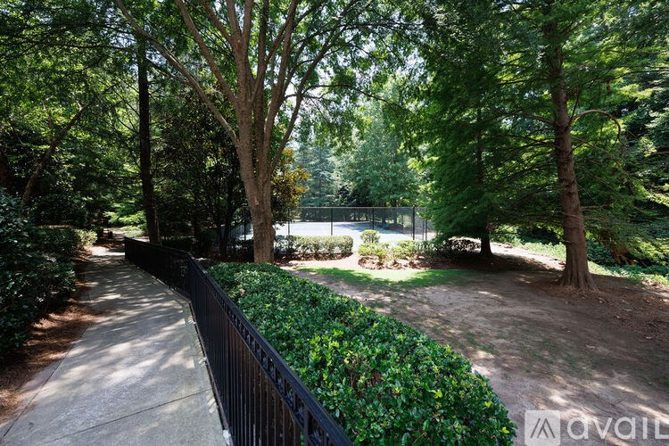 A pathway with a black fence and green trees on the side.