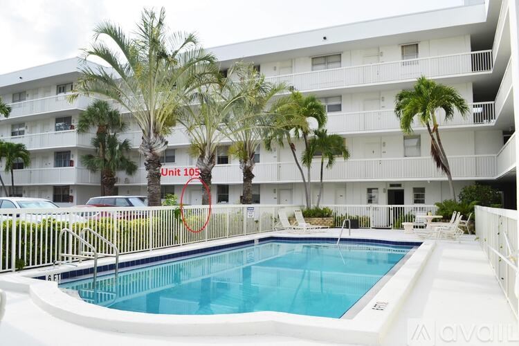 A swimming pool in front of a white building with palm trees.