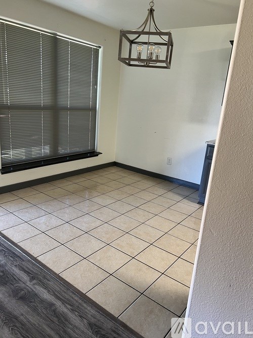 A room with a window covered by blinds and a chandelier hanging from the ceiling.