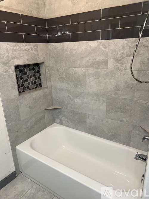 A white bathtub in a bathroom with grey tiles.
