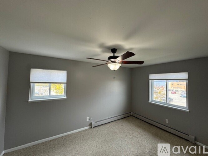 A room with a ceiling fan and two windows.