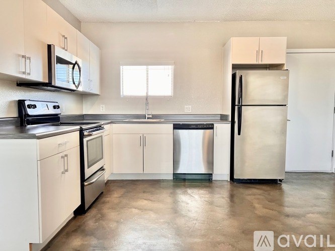 A kitchen with white cabinets and appliances, a window, and a trash can.