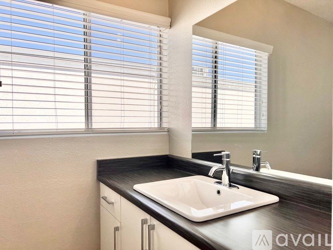 A bathroom with a sink, mirror, and window with blinds.