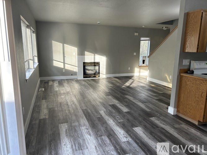A spacious room with wooden flooring and a staircase in the background.